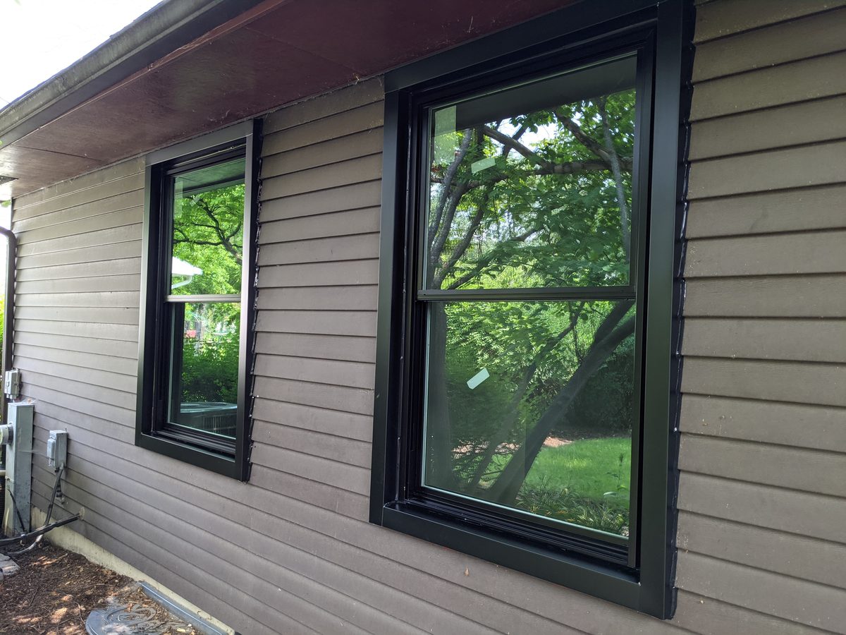 Two black replacement windows installed on a siding exterior